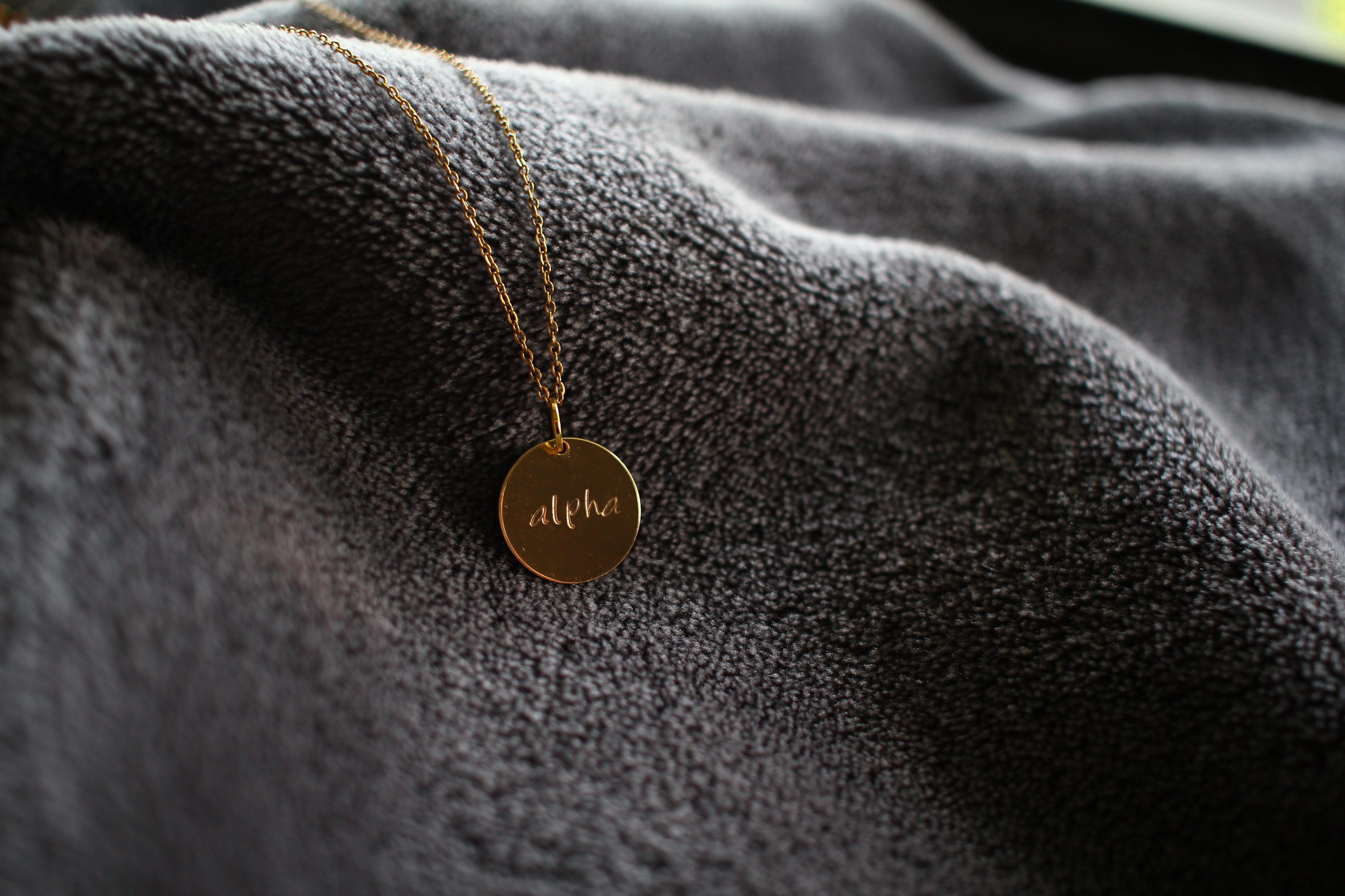 Gold necklace with 'Alpha' written on one side and 'Omega' written on the other side